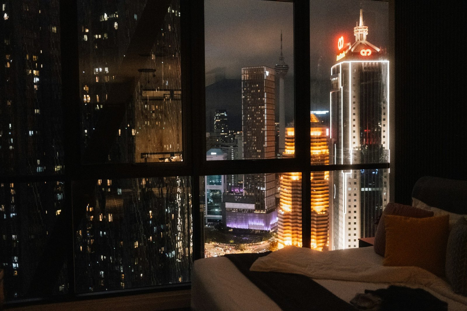 City skyline glowing at night through an apartment window, illustrating the challenge of sleeping with urban noise
