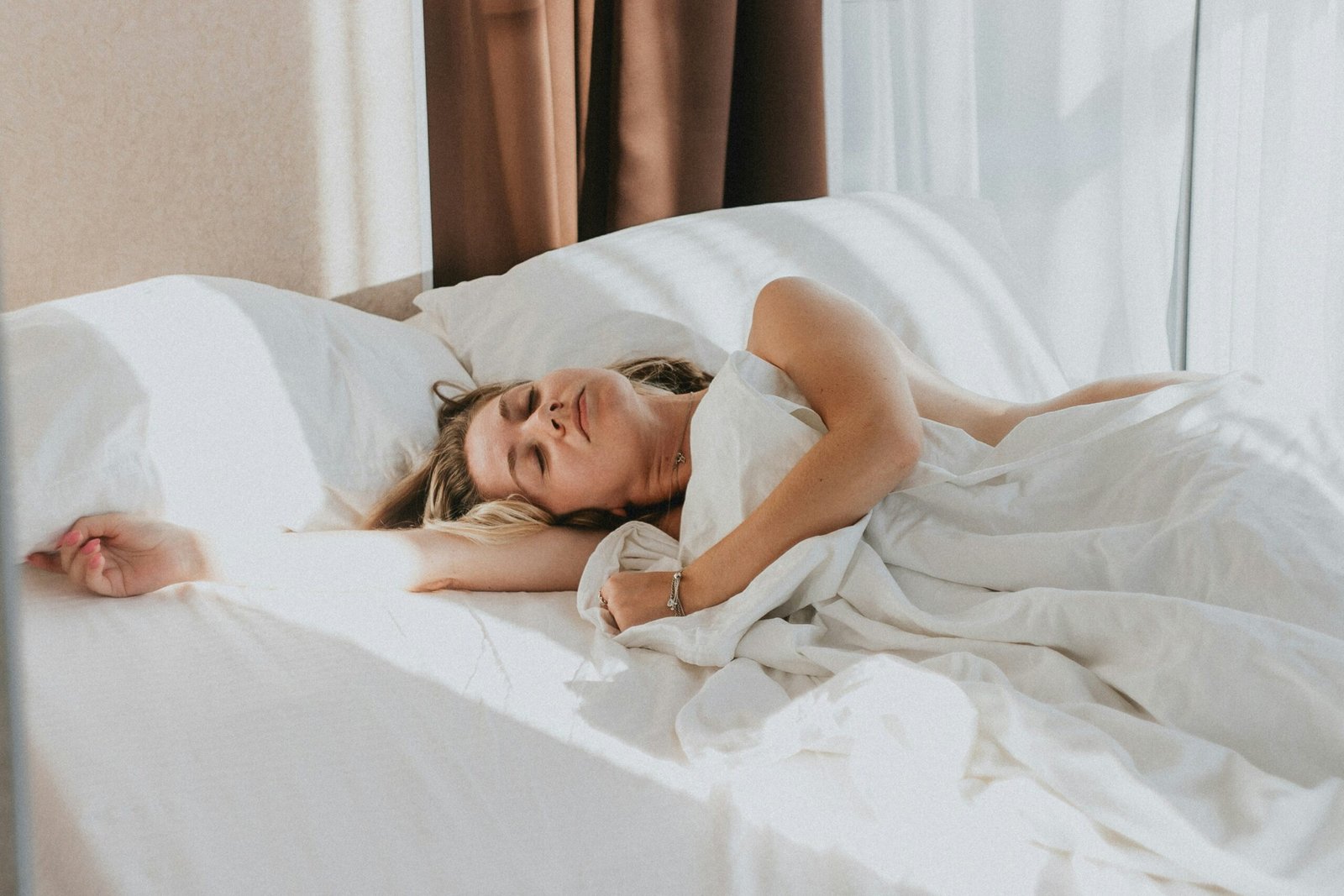 Person lying in bed under soft covers in a calm bedroom, illustrating rest and recovery